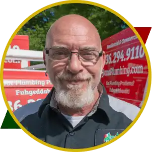 Smiling plumber with glasses and beard, wearing a black shirt with Bono Plumbing logo, background features red service vehicle, representing the family-owned plumbing team.